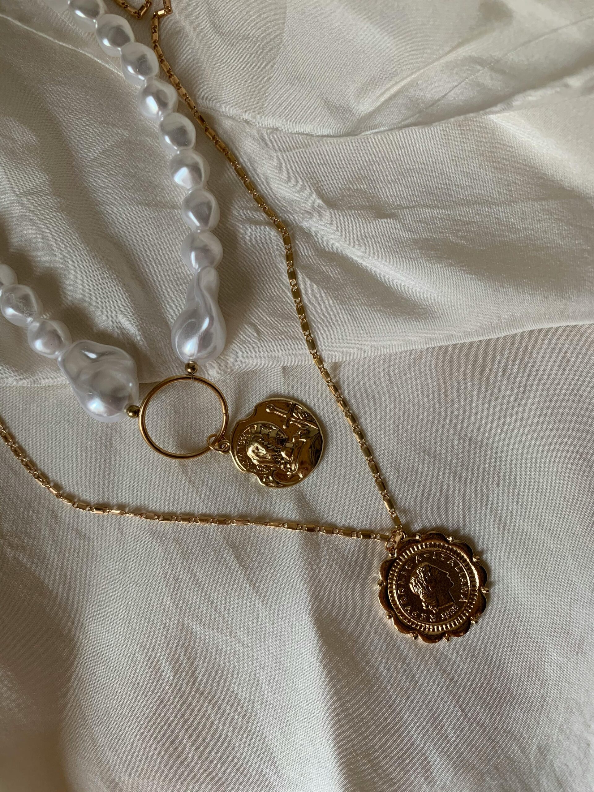 Stylish gold necklaces with pearls on soft fabric backdrop, showcasing luxury jewelry.
